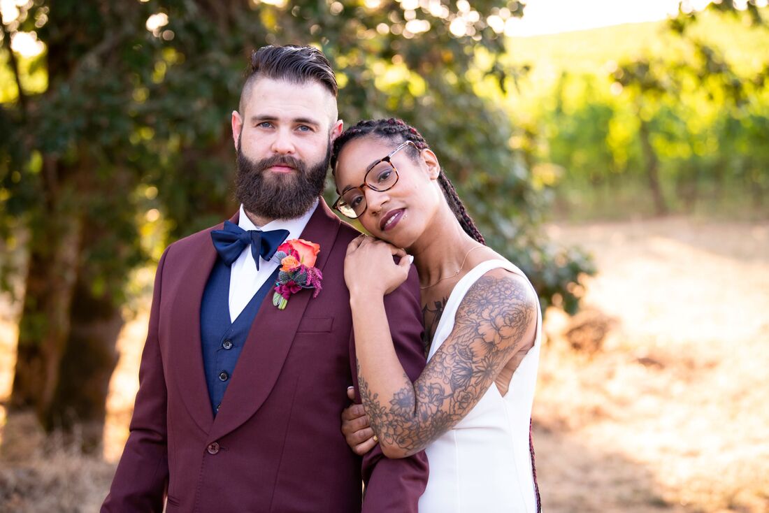 Groom in a burgundy tux with navy blue vest and tie. Bride leaning her head on his shoulder.